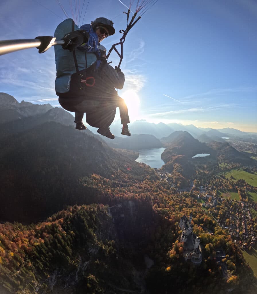 Tandem-Paragliding im Gegenlicht über Schloss Neuschwanstein und den herbstlichen Alpen bei Füssen im bayerischen Allgäu.